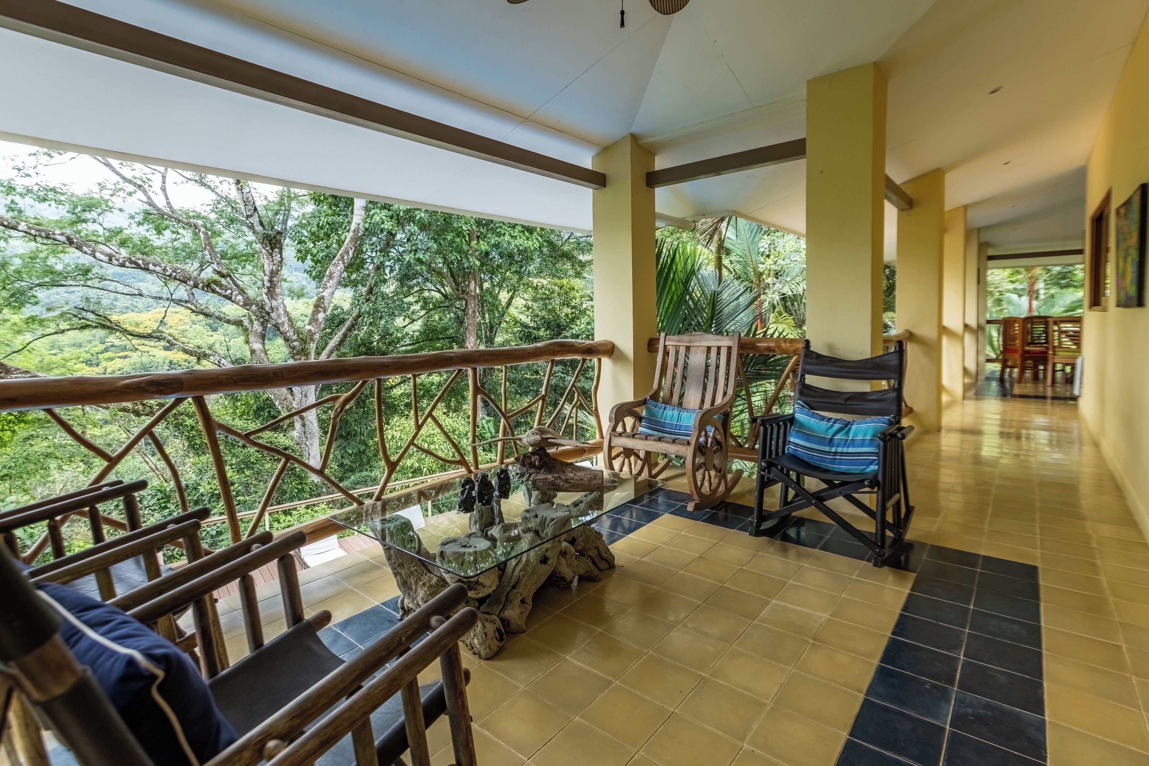 Um quarto espaçoso com mesa de vidro, cadeiras de madeira e vista para o verde exuberante lá fora.