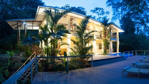 Une maison à deux étages dotée d’un balcon, entourée de plantes tropicales.