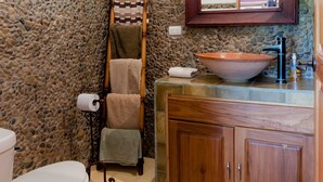 Une salle de bain avec un mur en pierre, une échelle en bois, des toilettes blanches, un meuble en bois et un grand miroir.