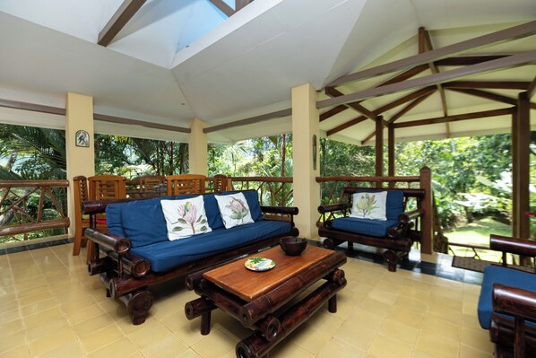 A covered outdoor seating area with wooden furniture and a tiled floor. - Monos Locos - Portasol Vacation Rental (Savegre)