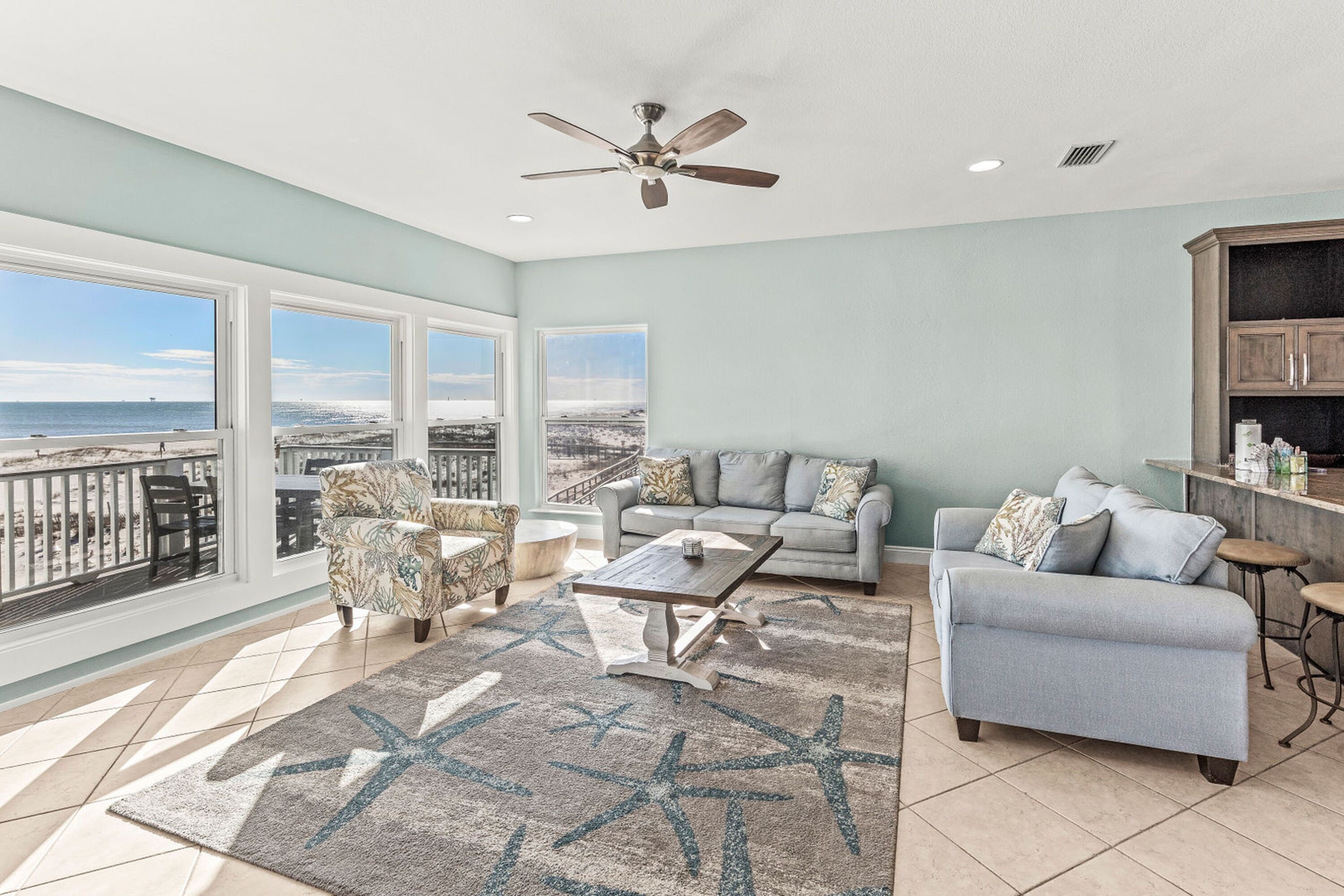 A spacious living room with a large window, a ceiling fan, and a view of the ocean.