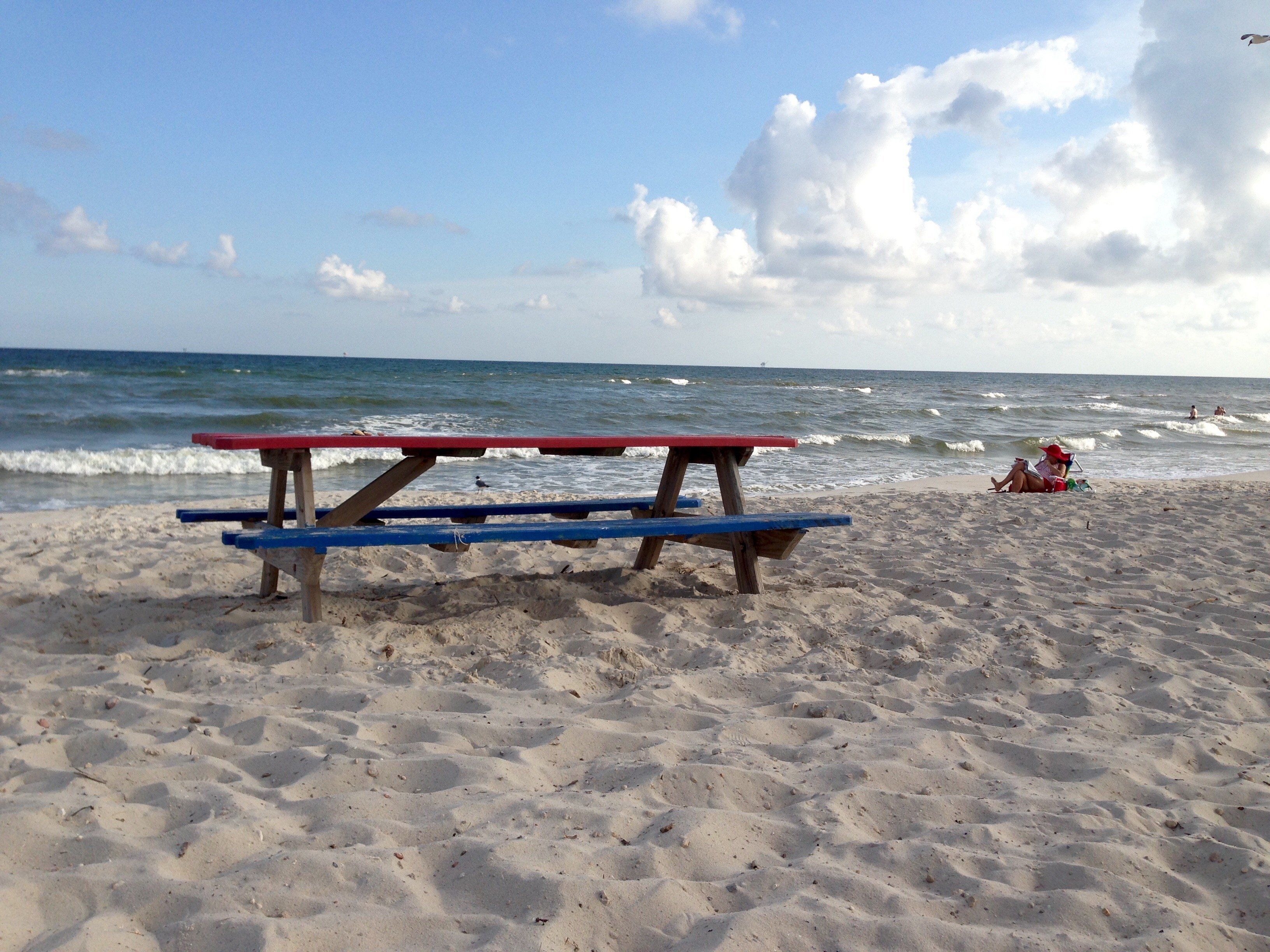 A beach with a wooden picnic table in the foreground and the ocean in the background.