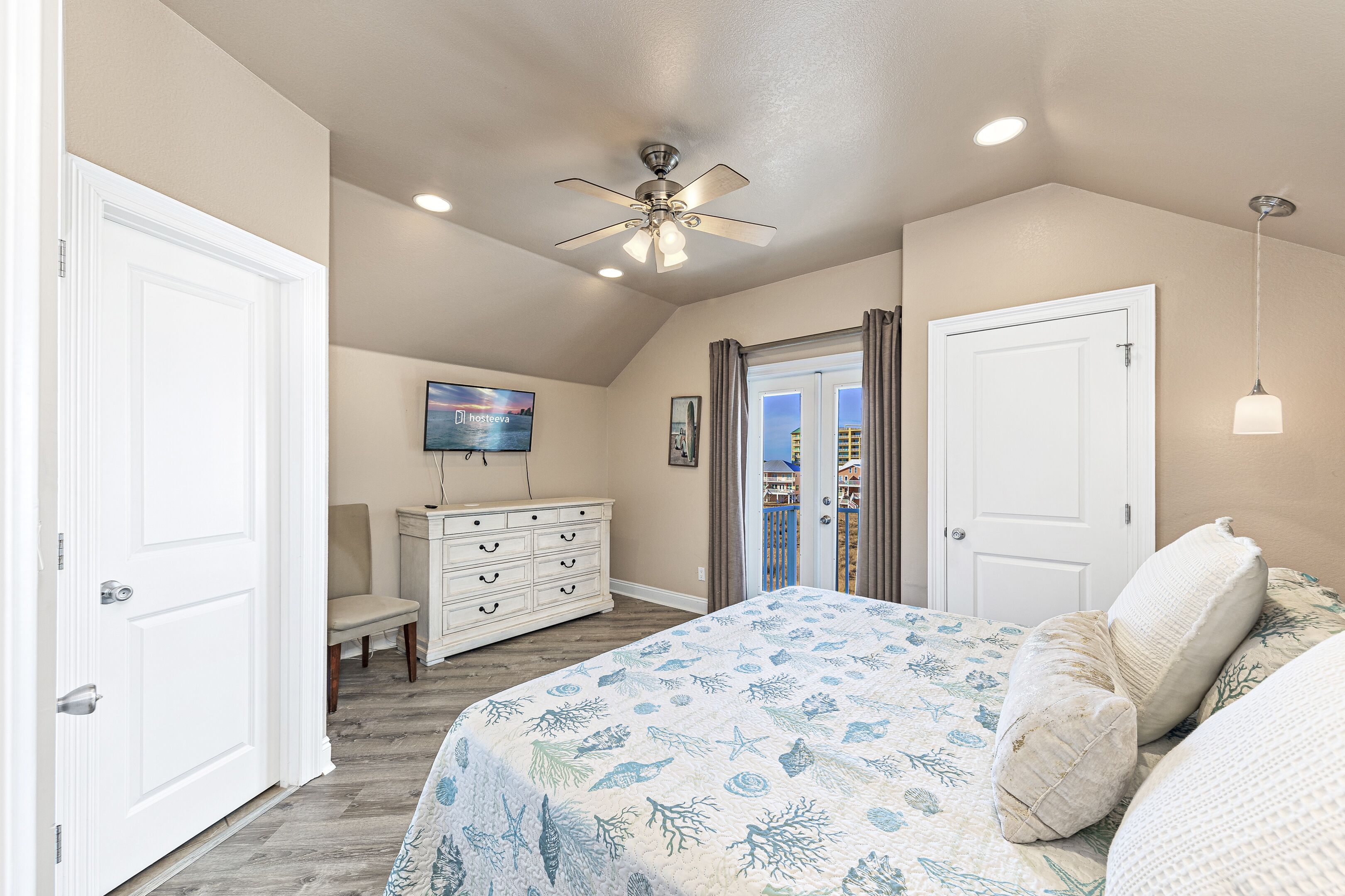 A bedroom with a bed, a ceiling fan, a dresser, a chair, and a door.