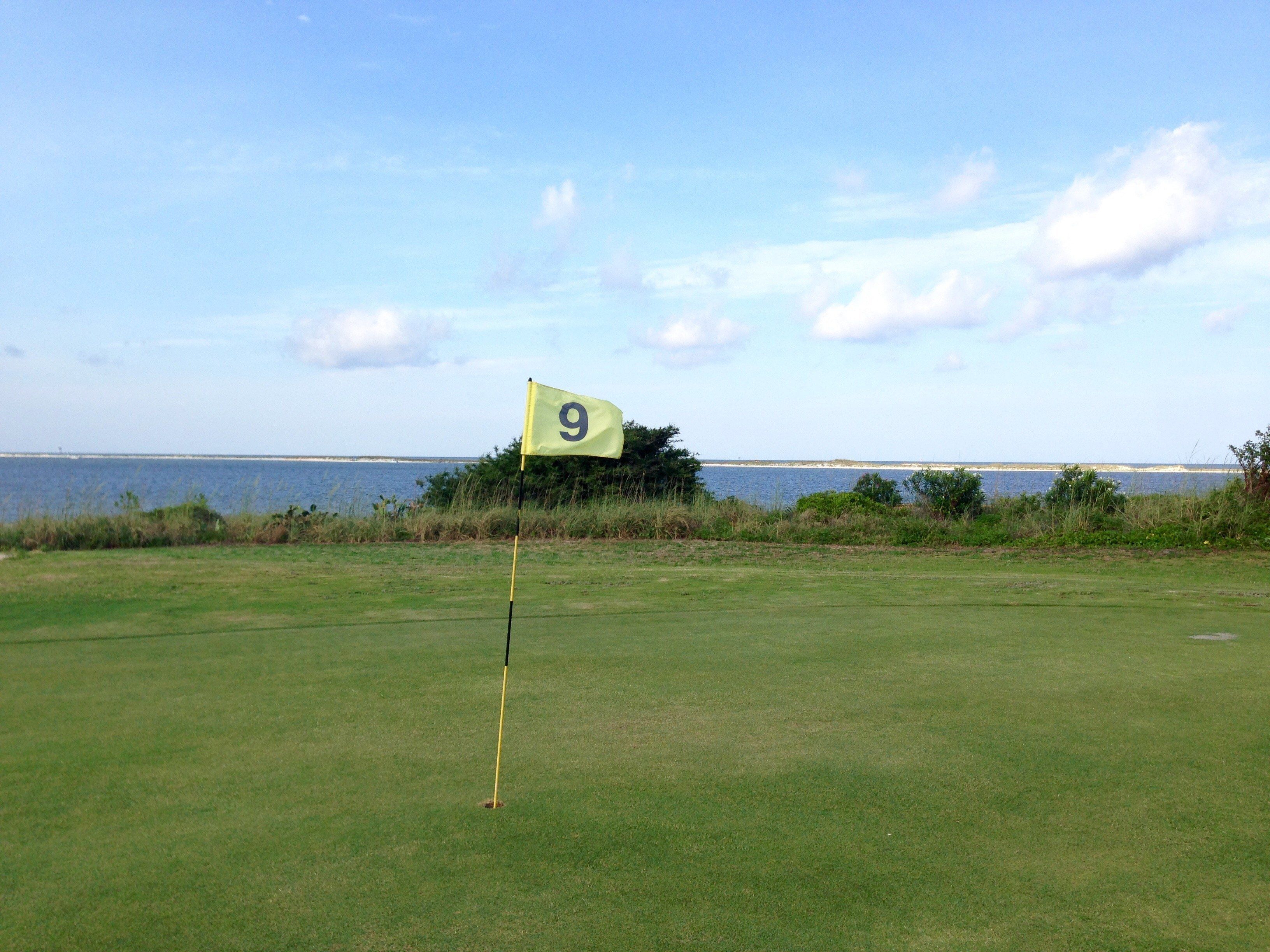 Un campo de golf con una bandera marcada con el número 9 en un green, cerca de una masa de agua.