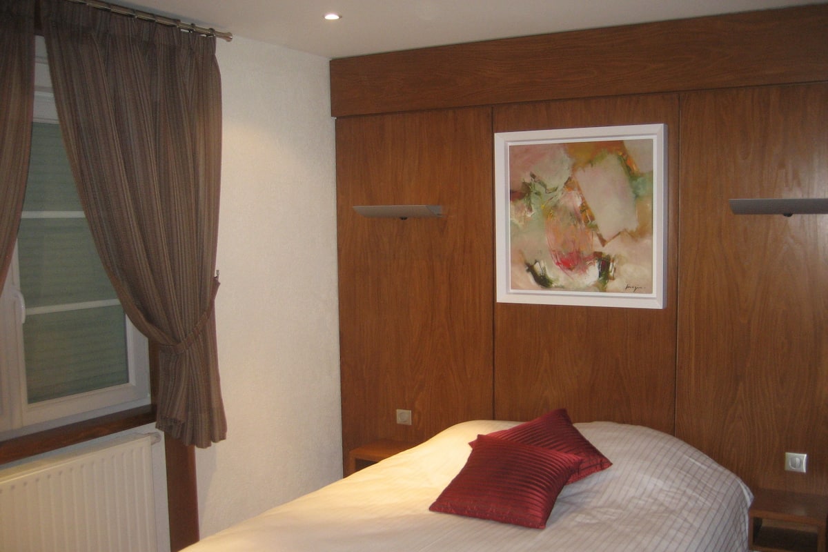 Ein Hotelzimmer mit Bett, Fenster mit Vorhängen, Heizkörper und einem Bild an der Wand.
