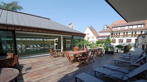 Una terraza en la azotea con piso de madera, mesas, sillas y sillones de descanso.