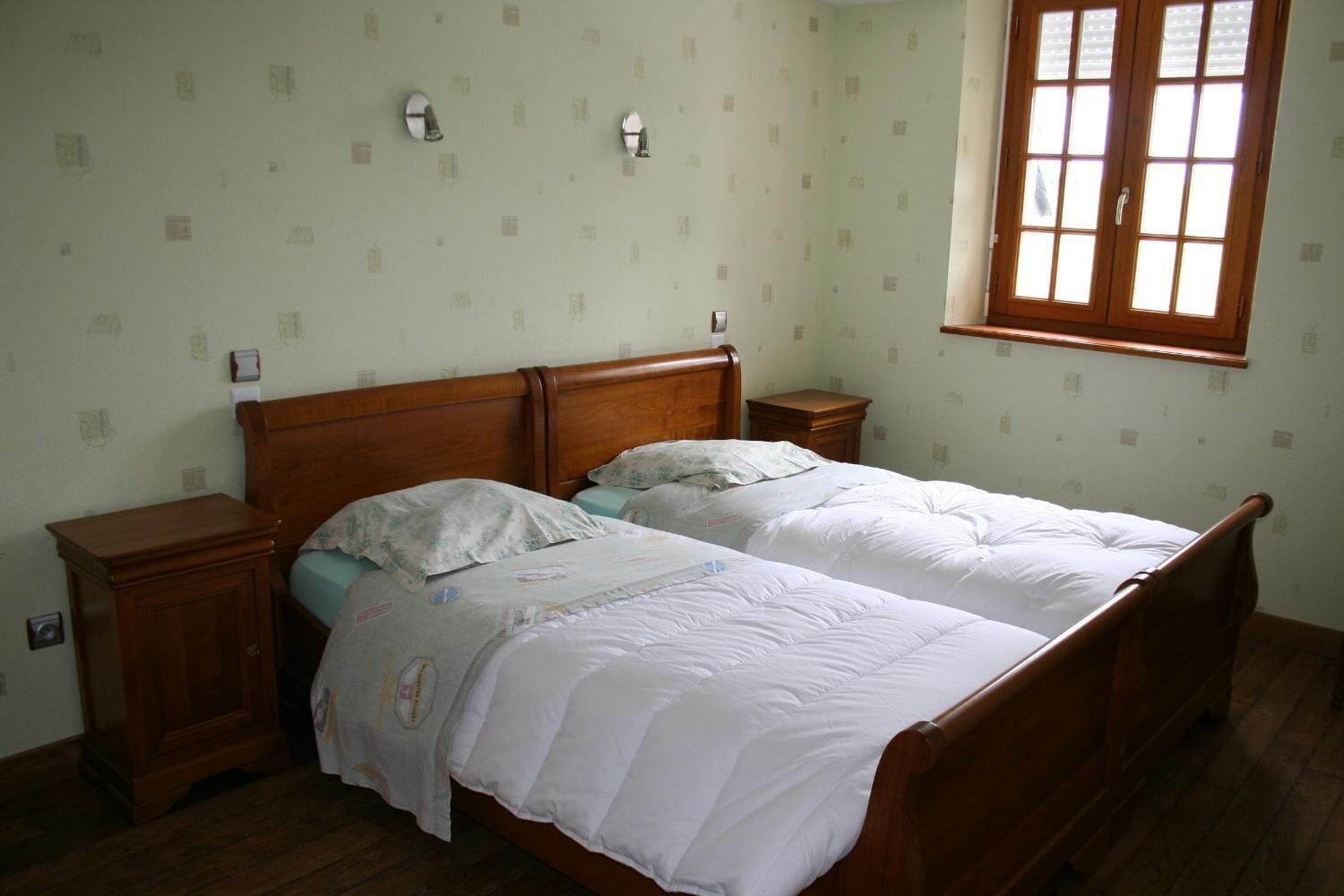 Un dormitorio con dos camas individuales, cabeceros de madera, mesitas de noche y una ventana con persianas.