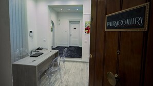 Un vestíbulo de hotel con mostrador de recepción, sillas traslúcidas, un letrero negro que dice "PALERMO GALLERY ART & SUITES" y una puerta con pomo de latón.
