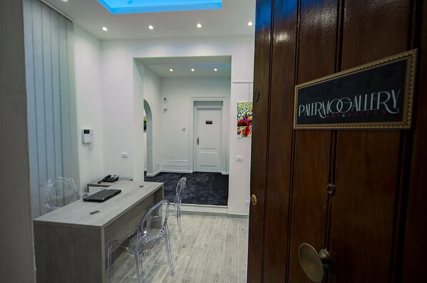 A hotel lobby with a reception desk, clear chairs, a black sign reading "PALERMO GALLERY ART & SUITES," and a door with a brass handle. - Palermo Gallery (Palermo)