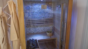 Una sala de sauna con estructura de madera, puerta de cristal y revestimiento interior de piedra.