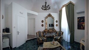 Una habitación con un espejo grande y ornamentado, dos sillones tapizados, una mesita de centro, una araña y un cuadro en la pared.