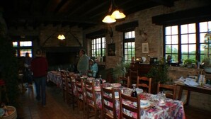 A rustic dining area with wooden tables and chairs, stone walls, and large windows allowing natural light. - Domaine des Garennes (Nadaillac)