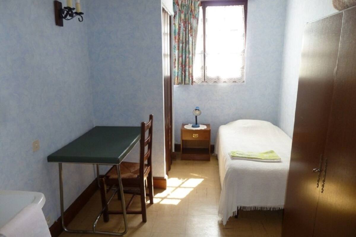 Une petite pièce simple, avec un lit, un bureau et une armoire.