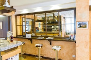 A bar area with a marble countertop, two stools, and a large window with shelves behind.