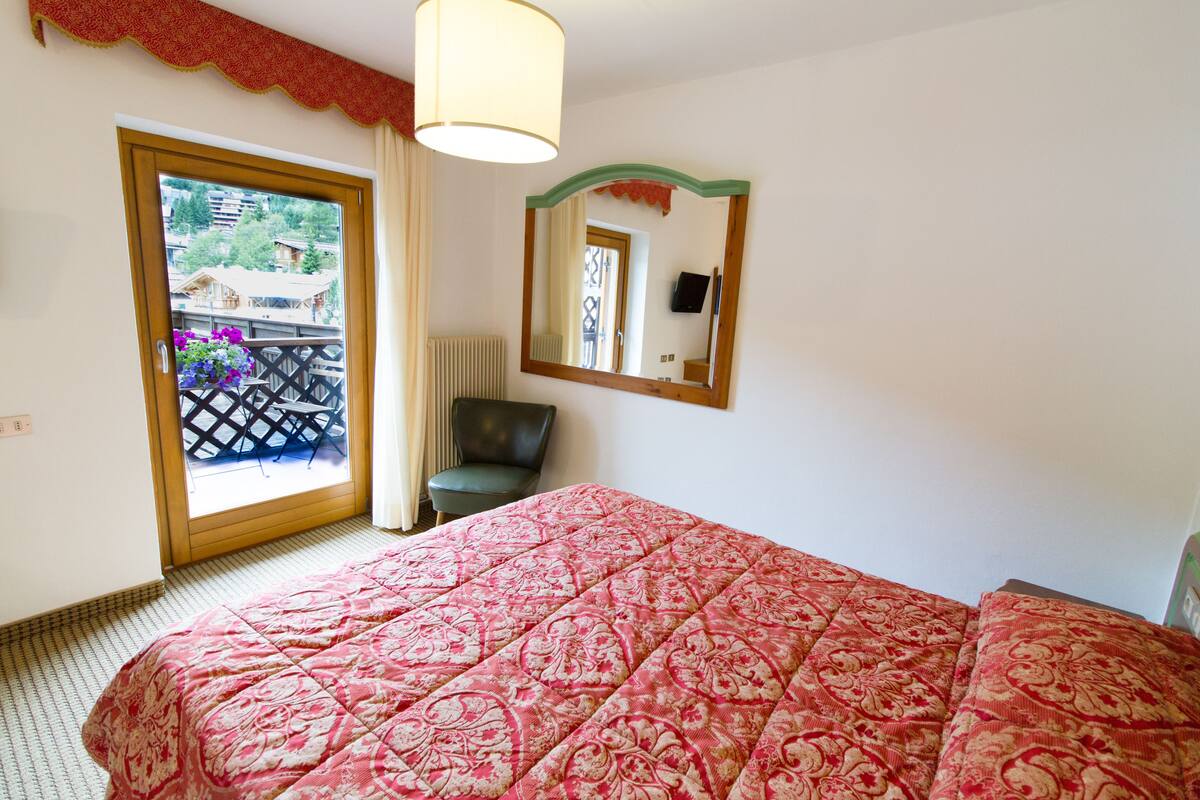 A hotel room with a large bed, a chair, a mirror, and a view of the outside balcony.