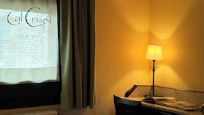 A room with a window, a lamp, and a chair. - Cal Crispí (Prades)