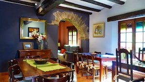 A dining area with a wooden table, chairs, a vase of flowers, a mirror, and a stone archway. - Cal Crispí (Prades)