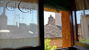 A window with a view of a building's roof and a bell tower. - Cal Crispí (Prades)