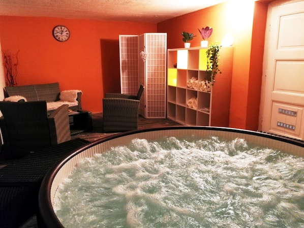 Une pièce avec un jacuzzi, une horloge au mur et une étagère où sont disposées des plantes.