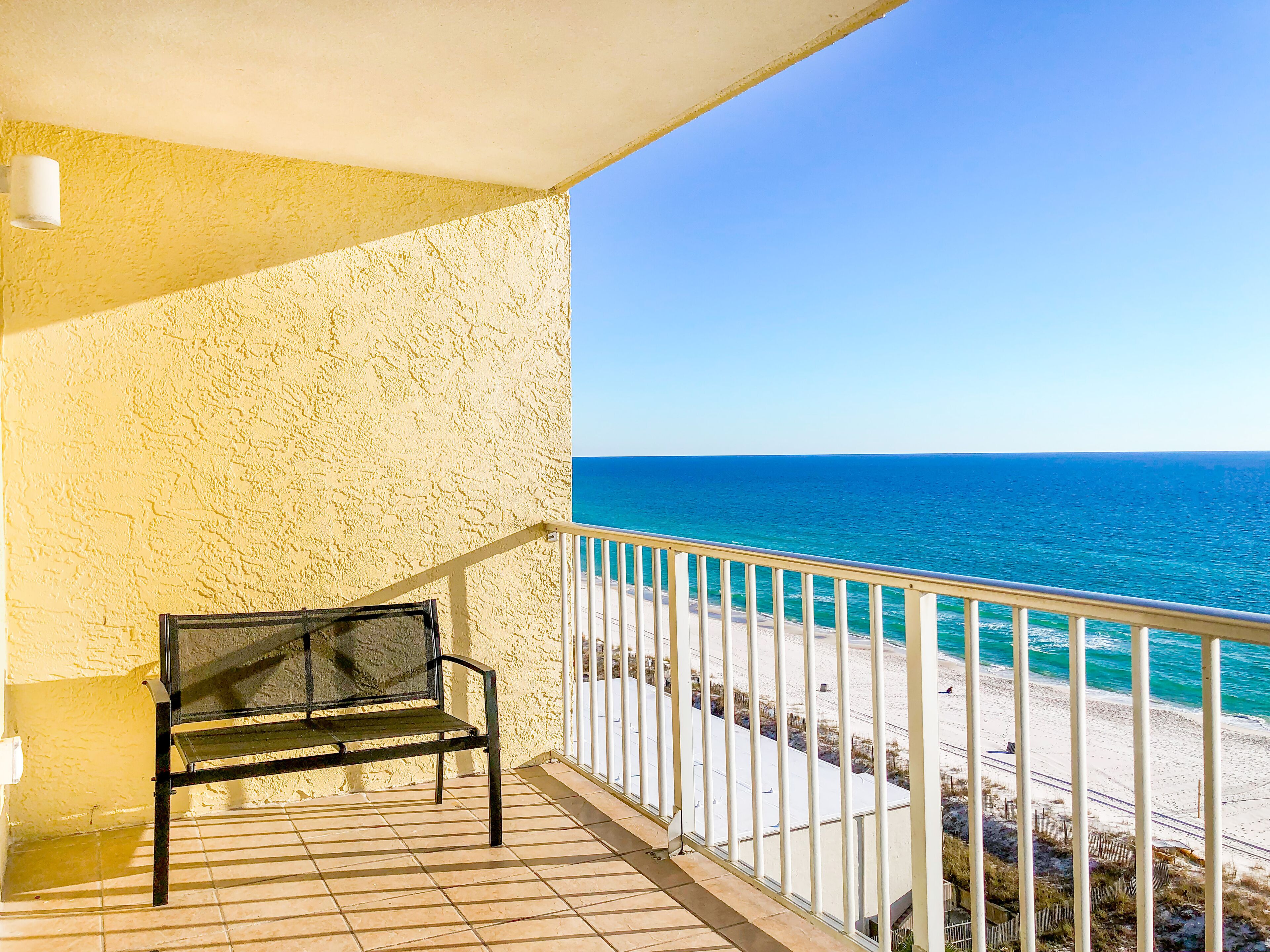 A balcony with a bench overlooking a beach.
