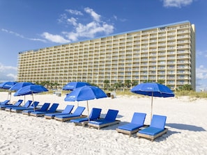 Ein Hotel mit mehreren Balkonen, einem Sandstrand und blauen Sonnenschirmen.
