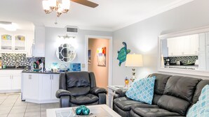 A modern living room with a leather sofa, a glass coffee table, and a kitchen in the background. - Summit Beach Resort by H2O VR (Panama City Beach)