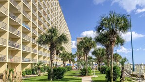 A hotel with a modern design, featuring a large building with multiple balconies and a well-maintained lawn with palm trees. - Summit Beach Resort by H2O VR (Panama City Beach)