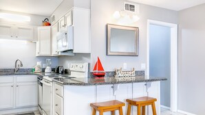 A modern kitchen with white cabinets, a granite countertop, a red toy sailboat, and two wooden stools. - Summit Beach Resort by H2O VR (Panama City Beach)