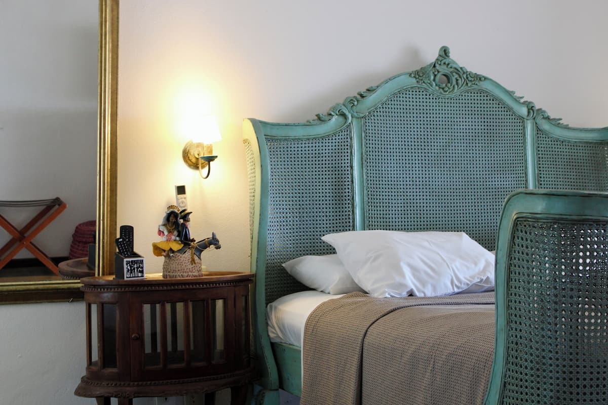 A room with a bed featuring a green headboard, a bedside table with a lamp, and a mirror on the wall.