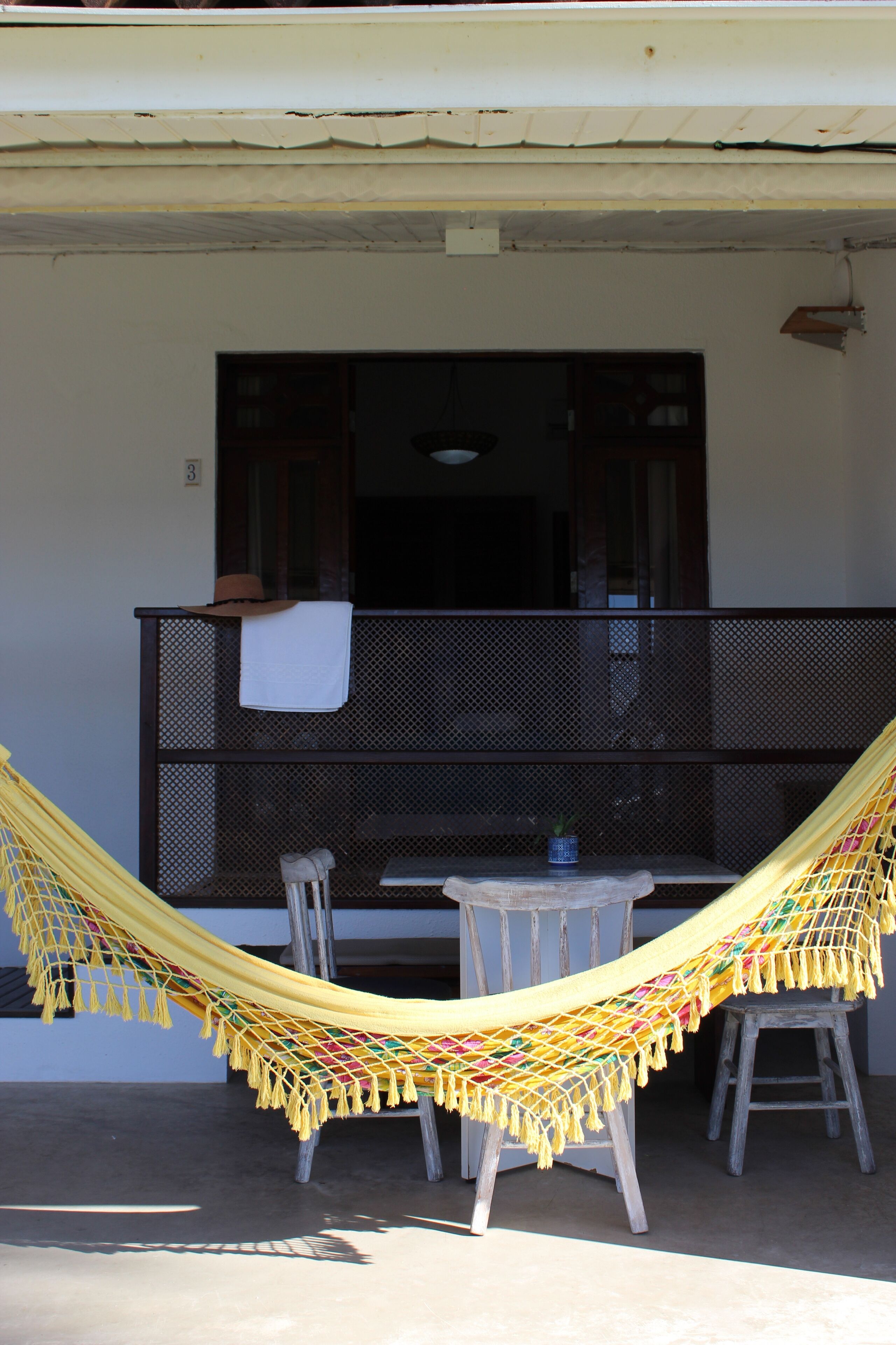 A balcony with a hammock, a small table, and a chair.