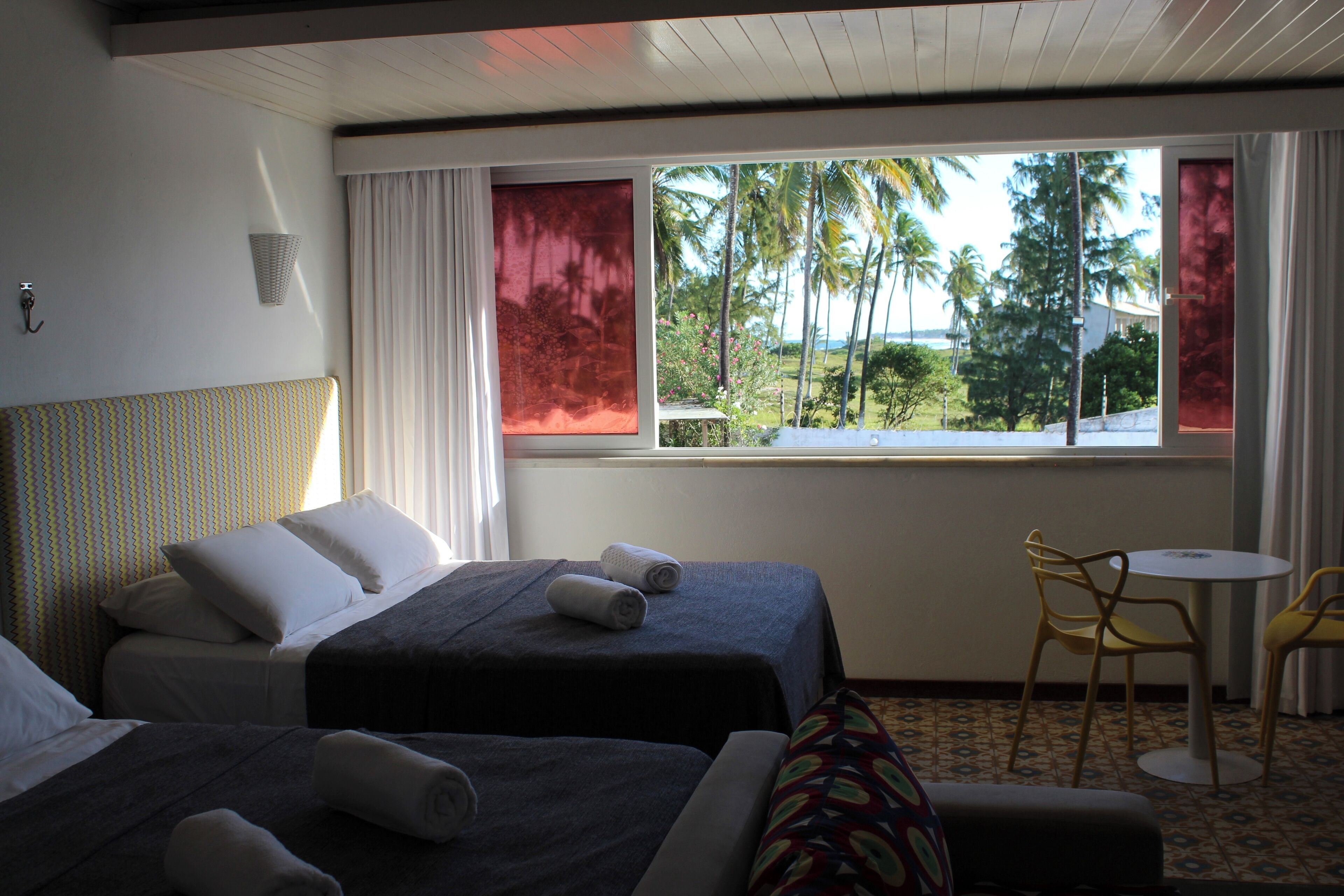 Quarto de hotel com duas camas, uma mesinha e uma cadeira.