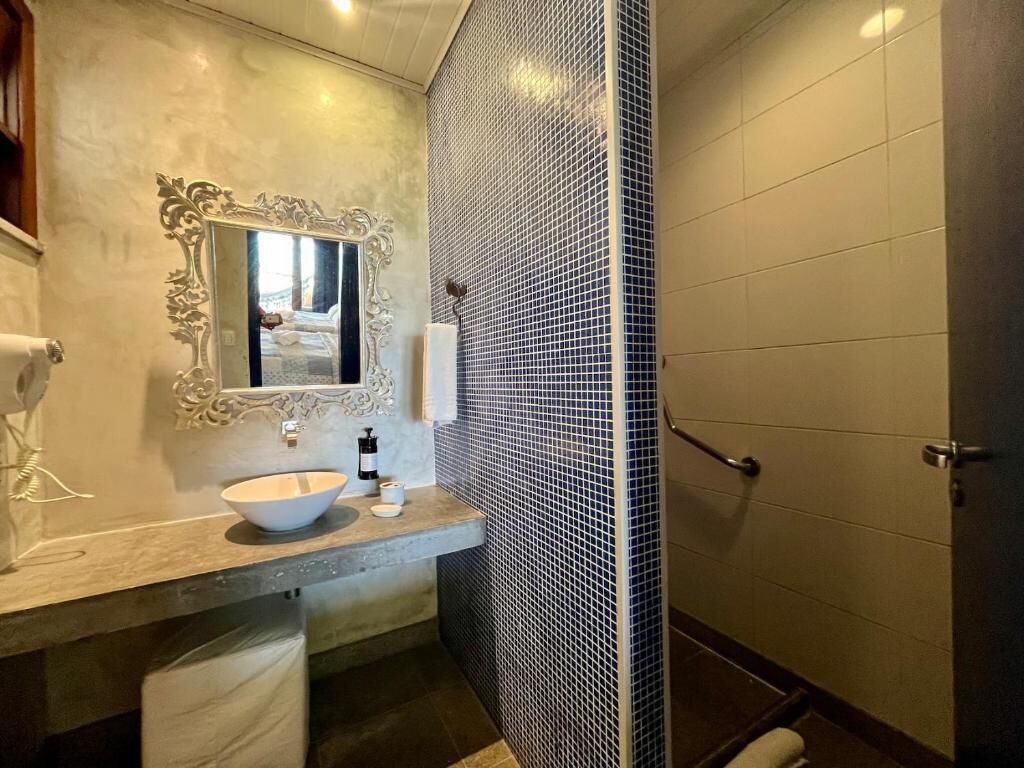 Casa de banho com lavatório de mármore, um espelho grande e cabine de duche revestida a mosaicos.