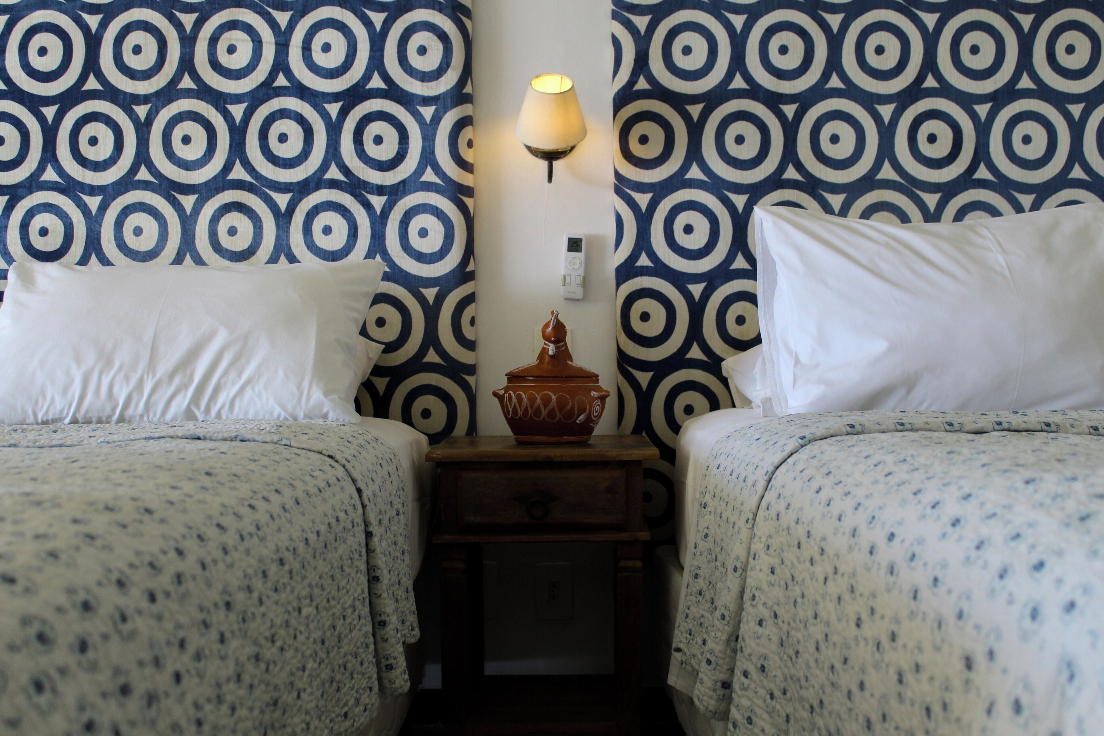 A room with two beds, a nightstand, a lamp, and a wall clock.