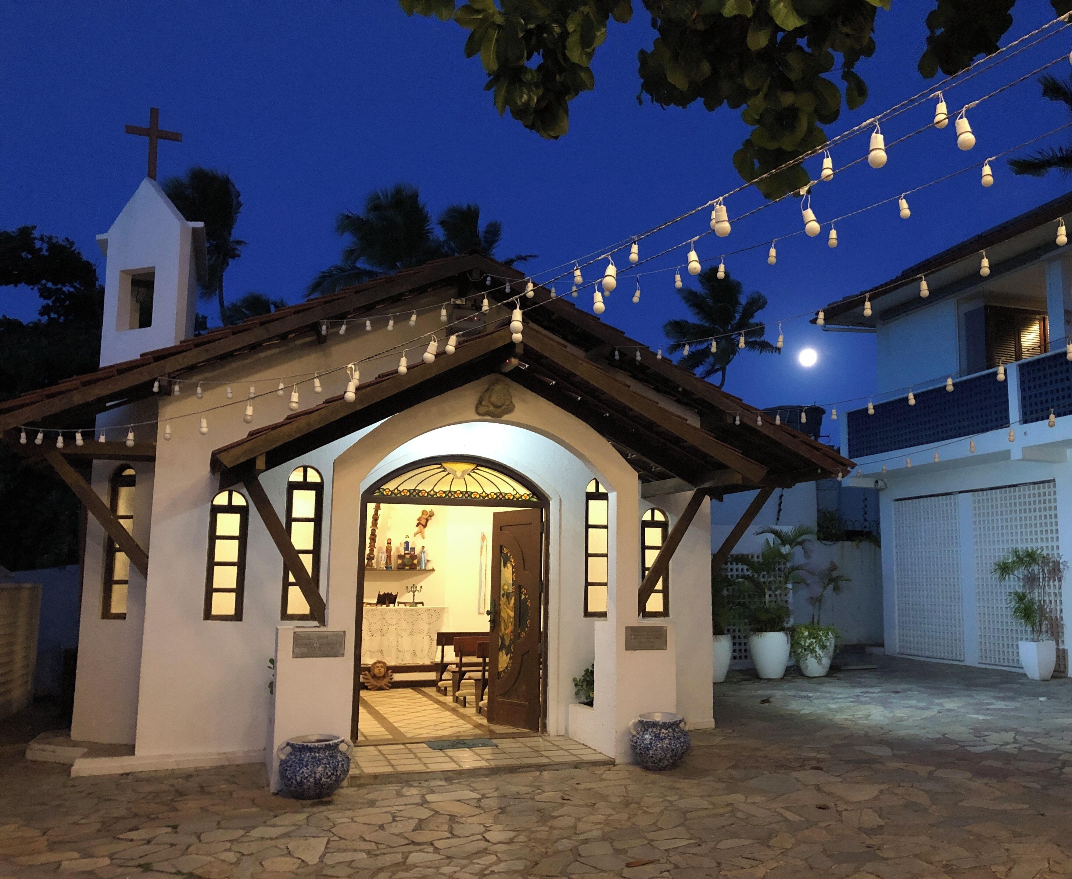 A small chapel with a cross on top, a wooden roof, and a welcoming entrance.