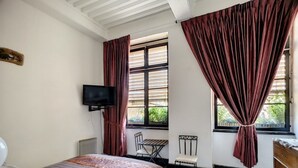 Un dormitorio con cama, televisor, ventana con cortinas, una mesita pequeña y una silla.