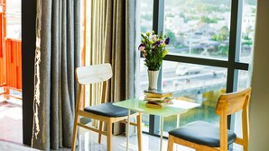 A room with a large window, a table with a vase of flowers, and two chairs. - Moonlight Bay Hotel (Bac Nha Trang)