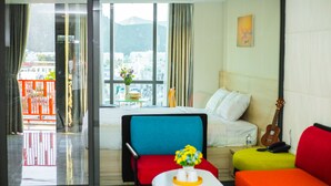 A hotel room with a bed, a colorful sofa, a small table with a vase, and a guitar. - Moonlight Bay Hotel (Bac Nha Trang)