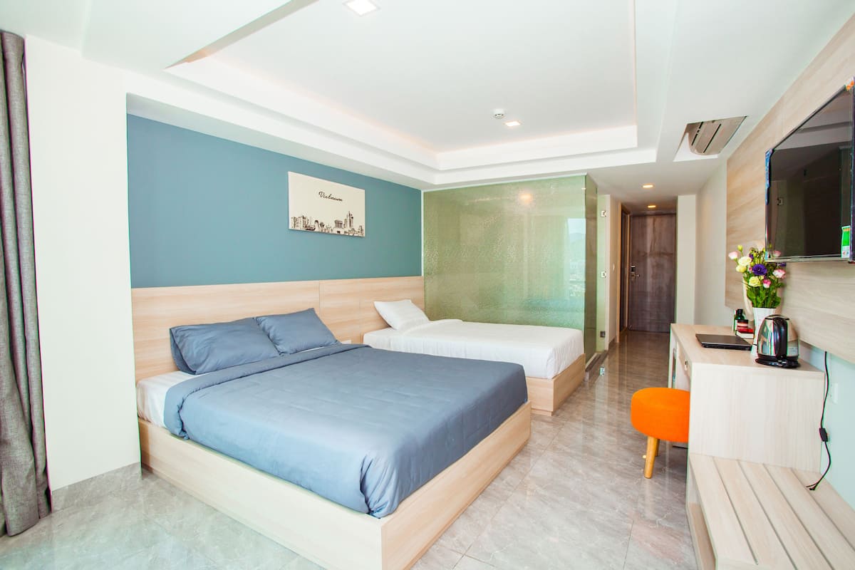A modern hotel room with a large bed, a smaller bed, a desk with a chair, and a mirror.