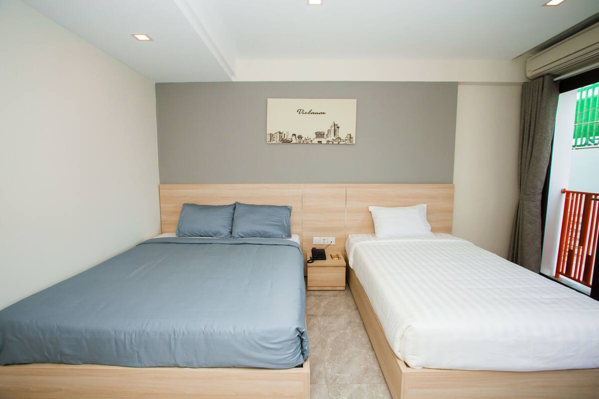 A hotel room with two beds, a cityscape wall art, and a window with a view.
