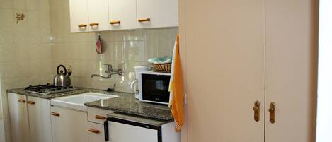 A kitchen with white cabinets, a stove, a sink, and a microwave.