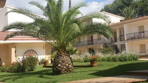 A courtyard with a palm tree, potted plants, and a building with balconies. - Apartaments Margarita Sabina Pinell (Castell-Platja d'Aro)