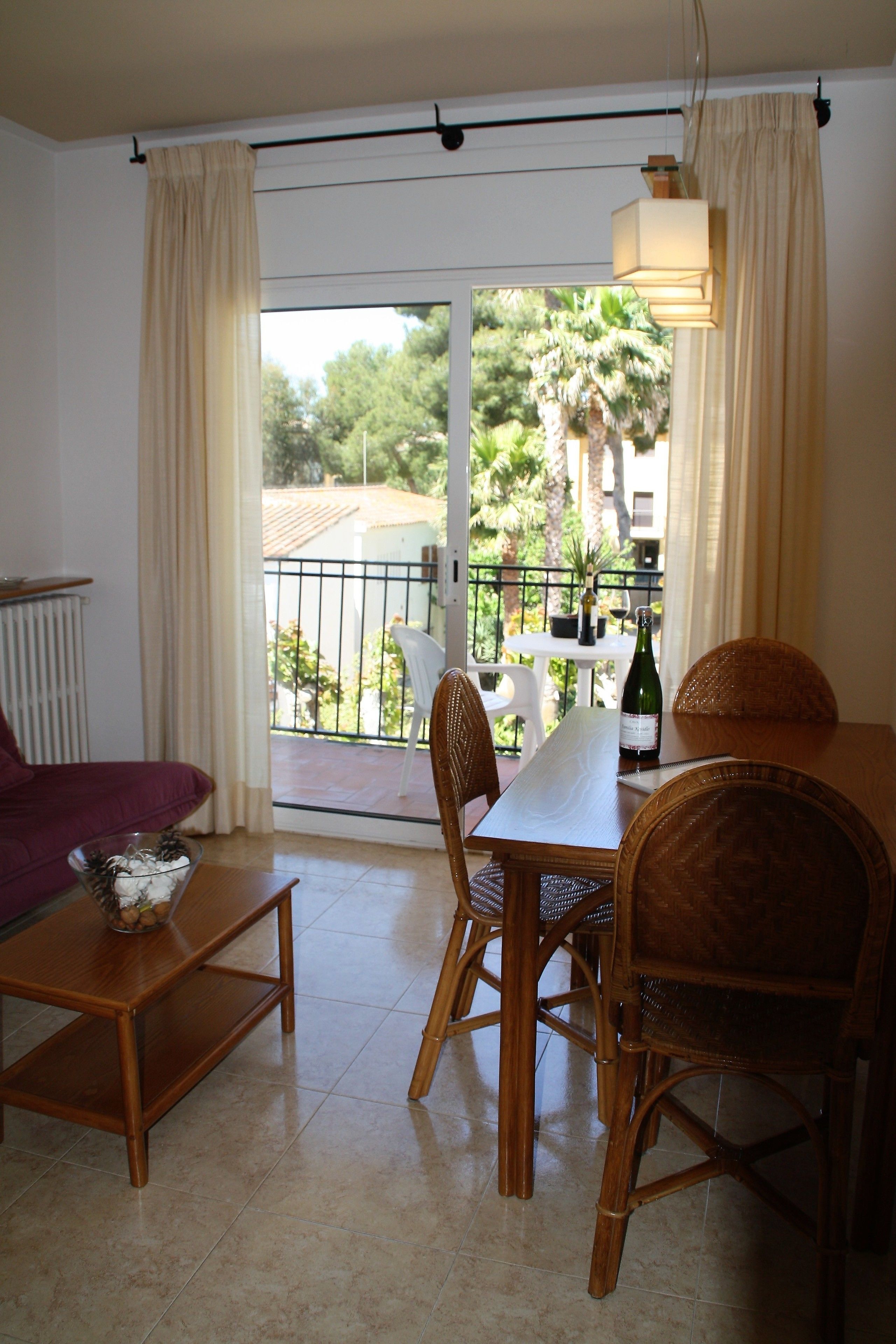 Un coin repas avec une table, des chaises et une bouteille de vin, situé sur un balcon offrant une vue sur la verdure et les bâtiments.