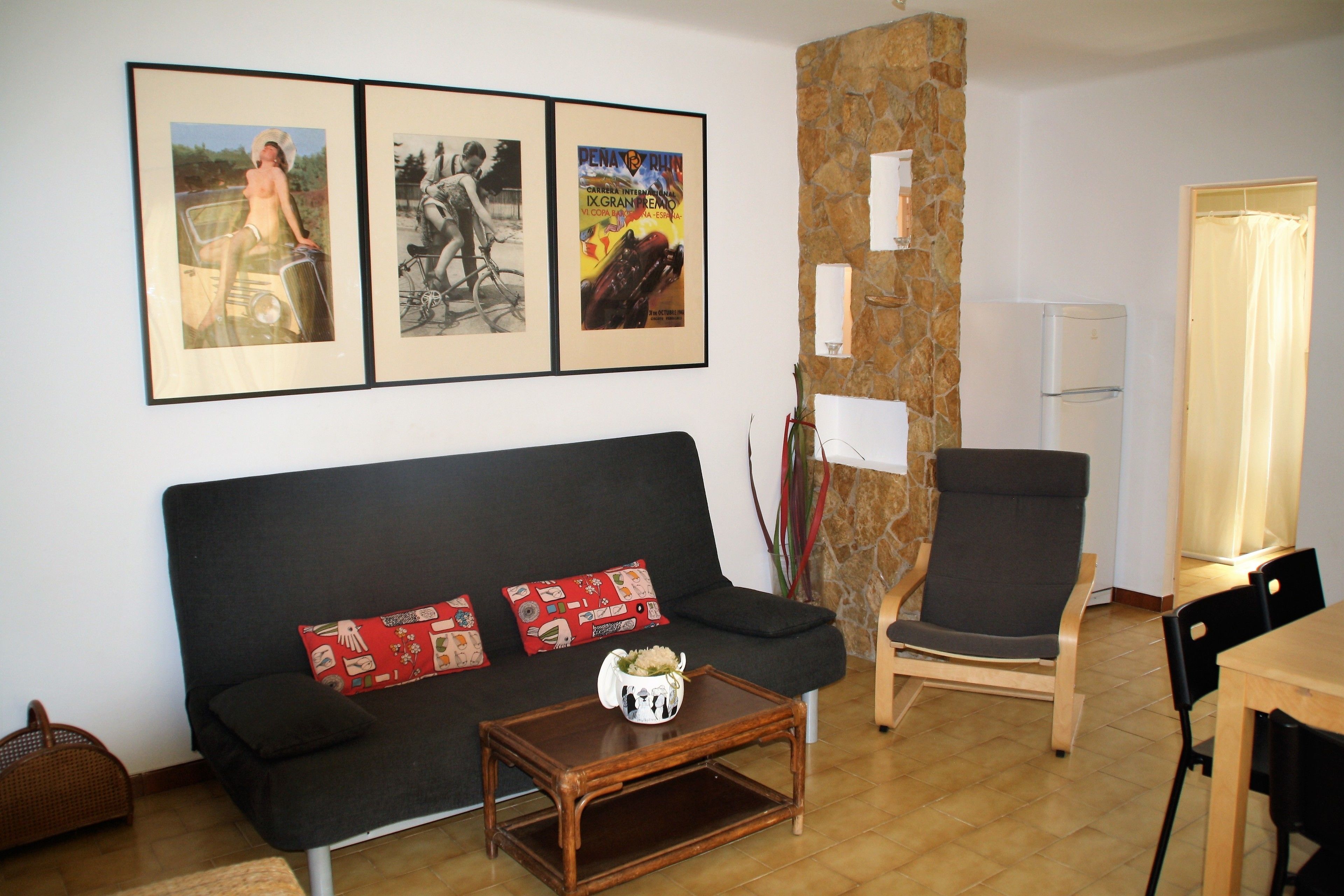 A living room with a black sofa, a wooden coffee table, a stone pillar, a black armchair, and a dining table with chairs.