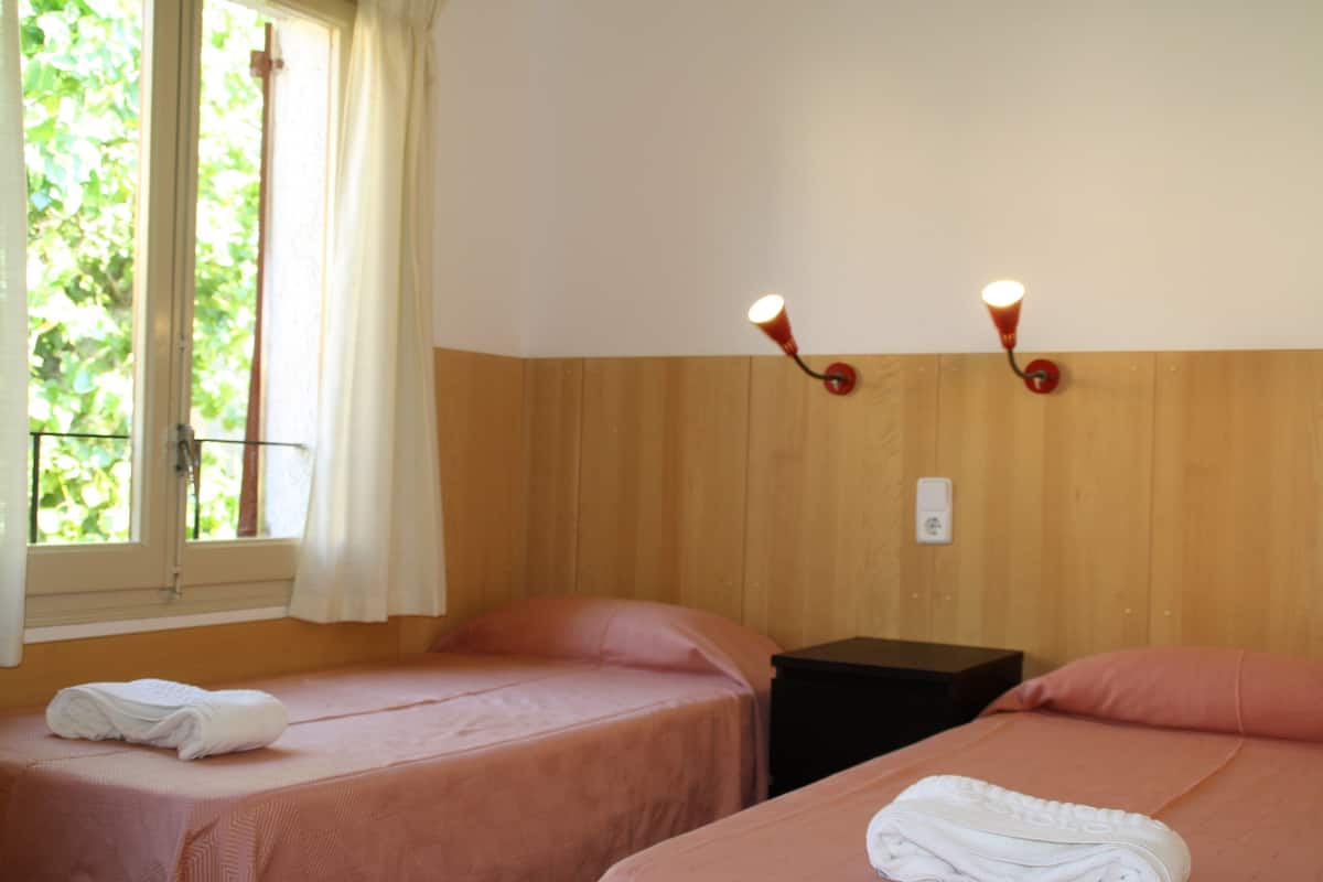 Una habitación con dos camas, una ventana con cortinas e iluminación en la pared.