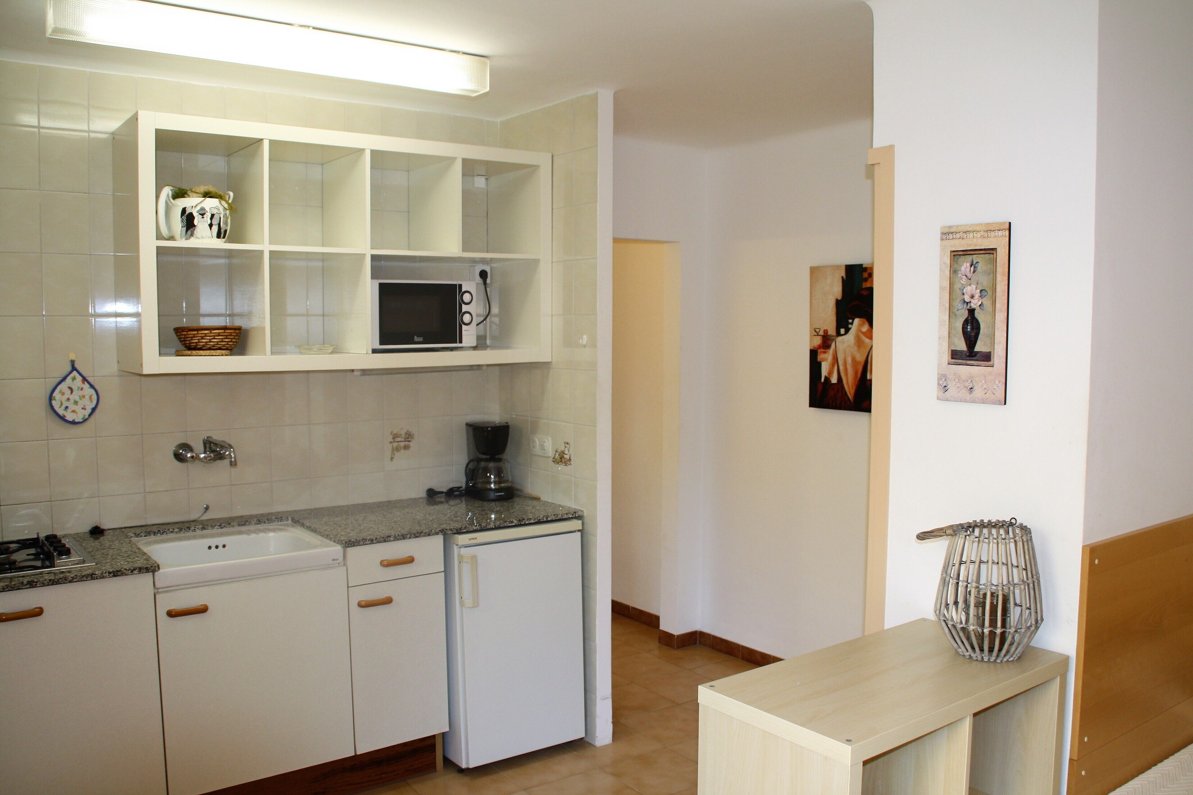 A kitchen with white cabinets, a microwave, a coffee maker, and a sink.