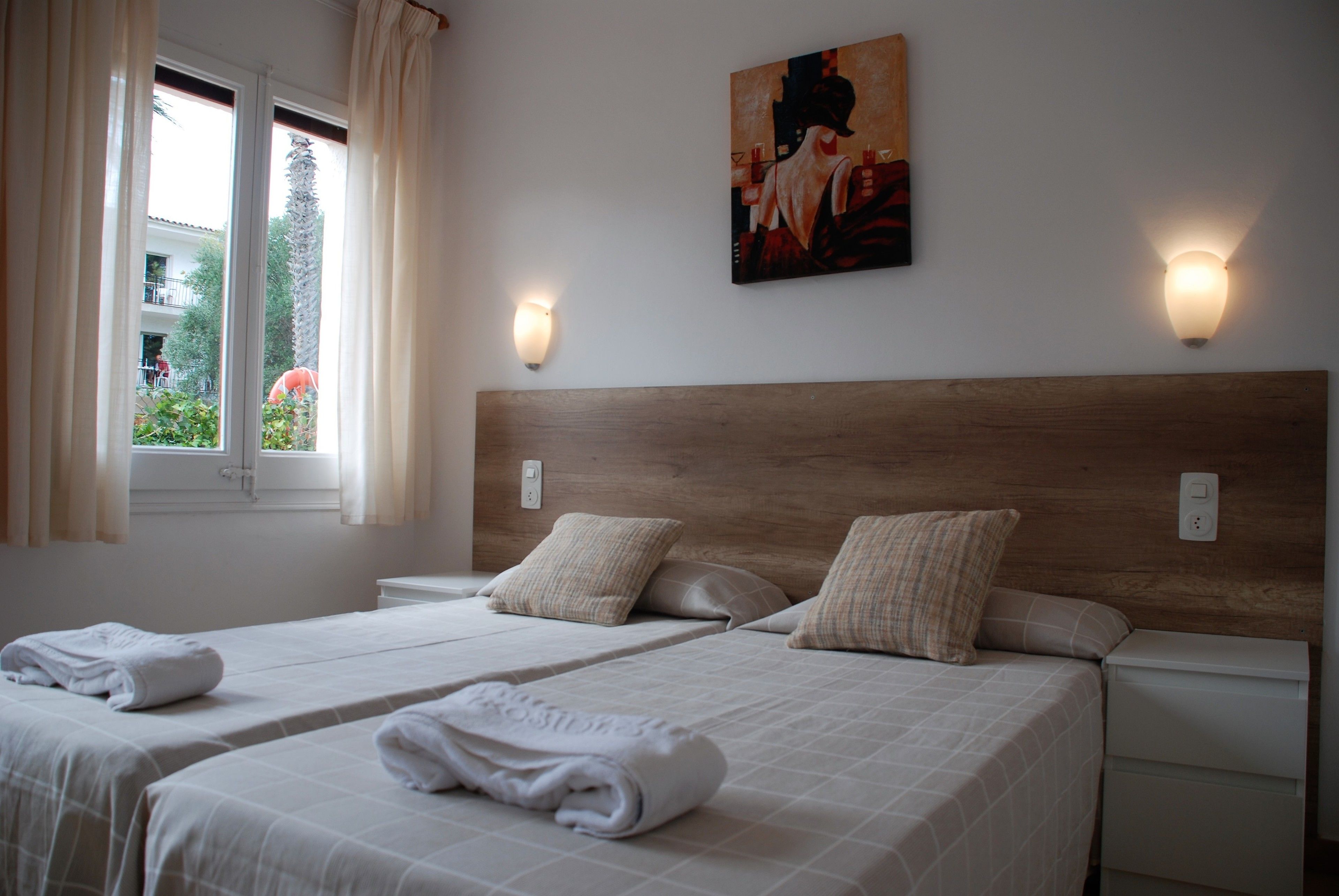 Une chambre d’hôtel avec deux lits, une tête de lit en bois, des lampes fixées au mur et un tableau.