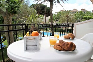 Een ronde tafel met ontbijtartikelen, waaronder croissants, sinaasappelsap en een fruitmand.