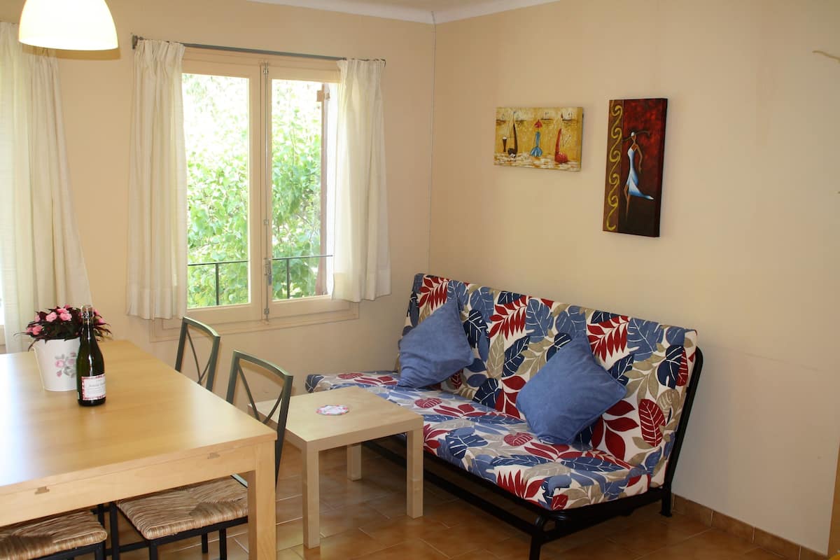 Un área de comedor con una mesa y sillas de madera, un sofá con tapicería floral y dos cuadros en la pared.