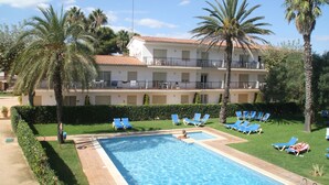 A hotel with a swimming pool, palm trees, and a balcony with lounge chairs. - Apartaments Margarita Sabina Pinell (Castell-Platja d'Aro)
