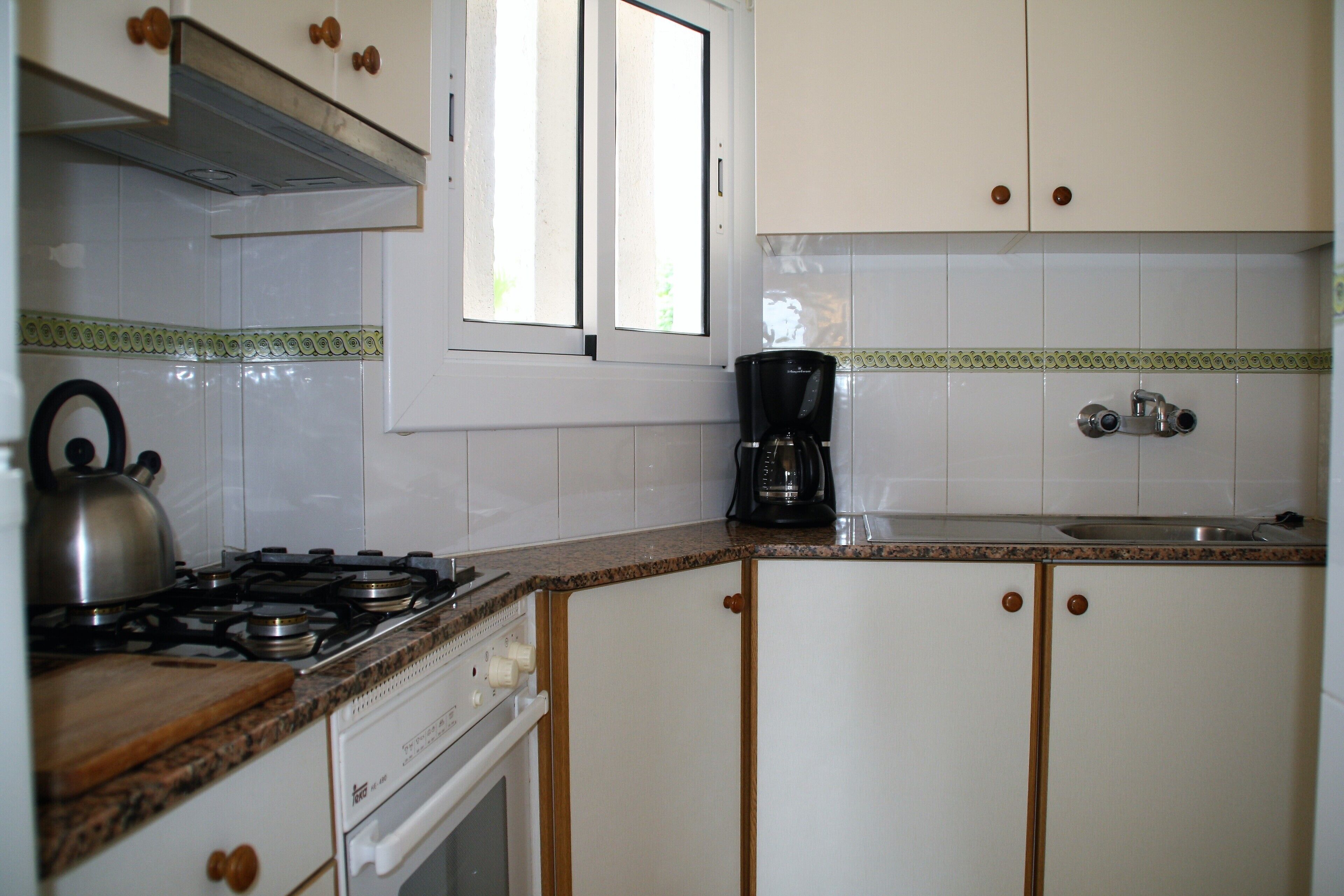 Une cuisine avec des meubles blancs, une cuisinière, une machine à café et une fenêtre.